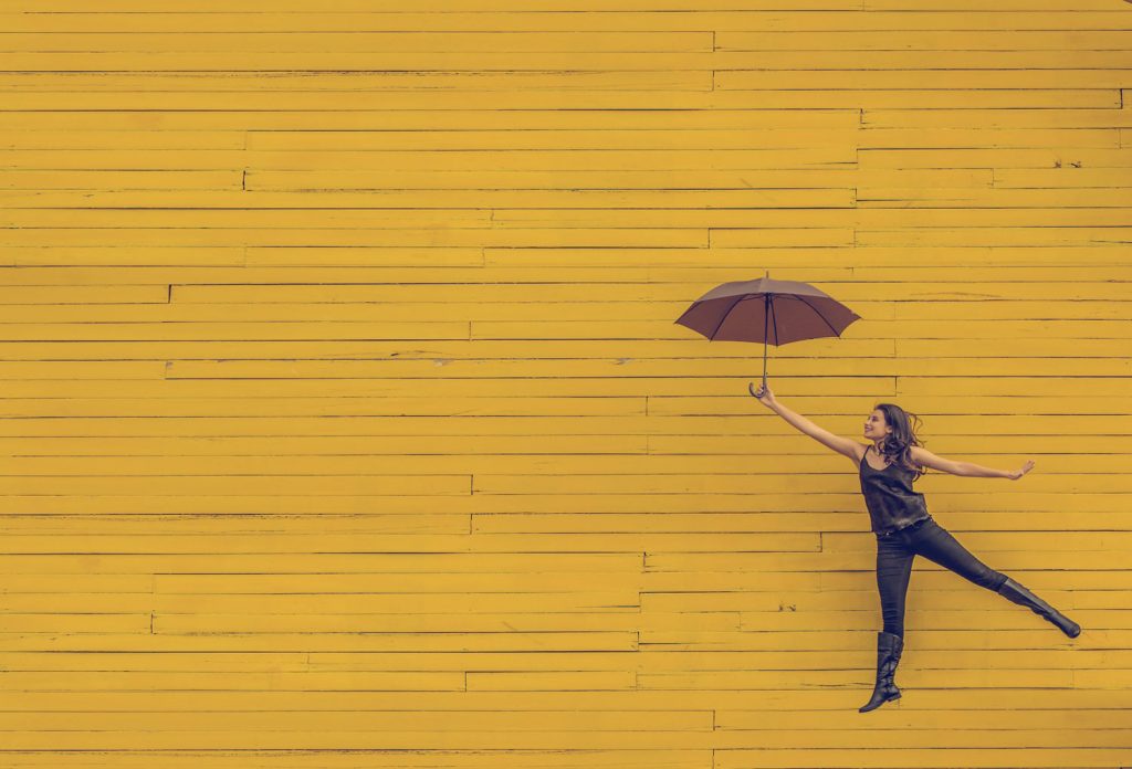 woman-jumping-with-umbrella-yellow-wall