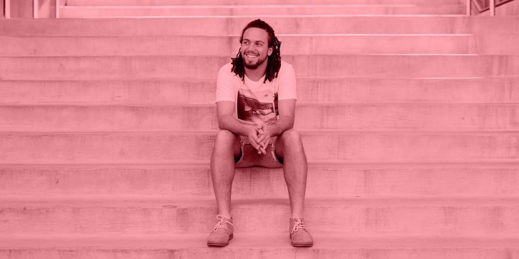 A grinning man sits on the steps to a building