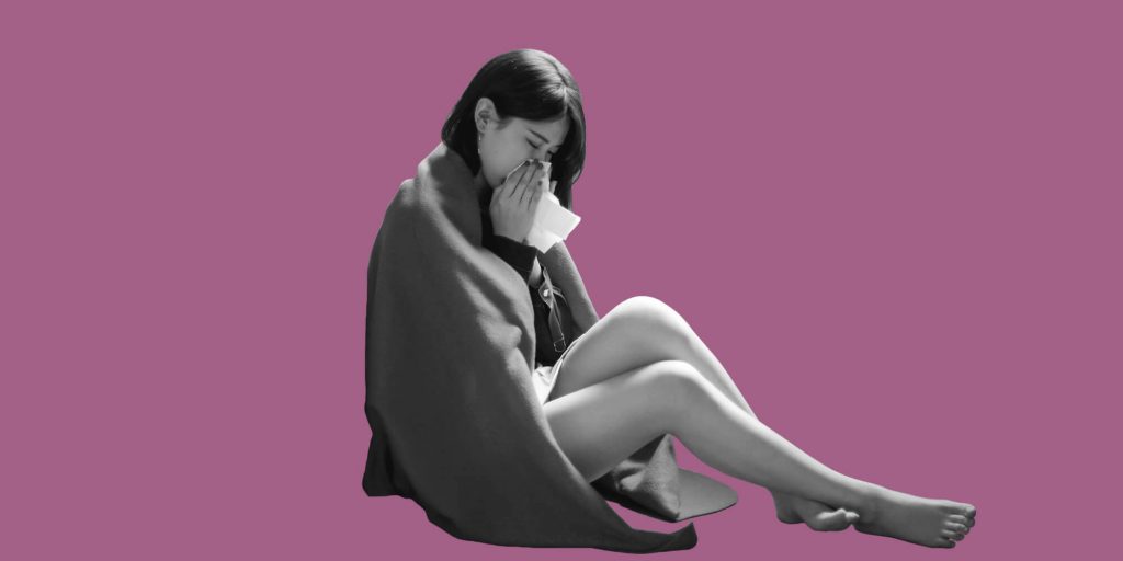 A woman wrapped in a blanket blowing her nose. Staying sober when you're sick.