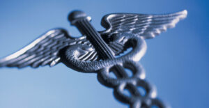 A silver-colored metal caduceus (the medical symbol that is two snakes wrapped around a winged staff) on a blue background.
