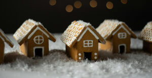 A row of small, simple gingerbread houses on a table strewn with fake snow.