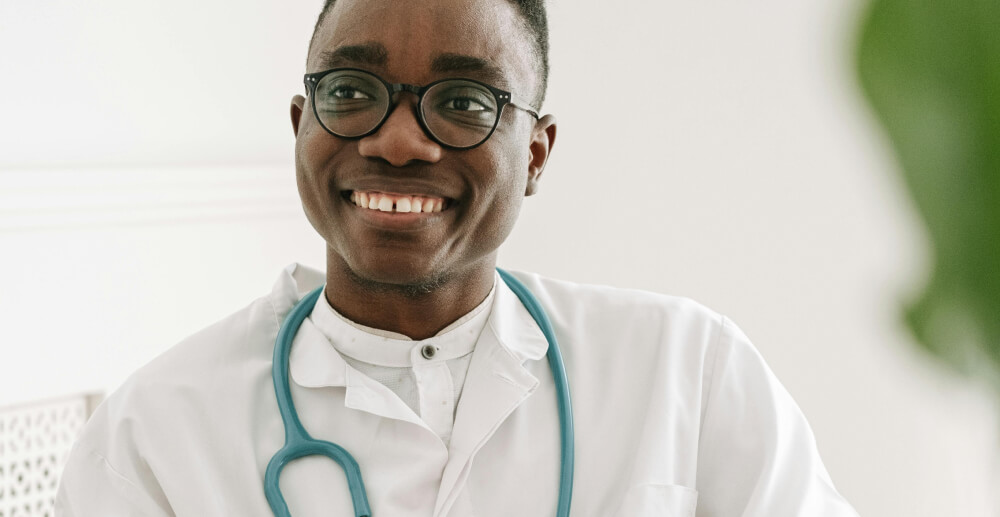 Young, Black, male doctor with a stethoscope around his neck smiles at someone off-camera