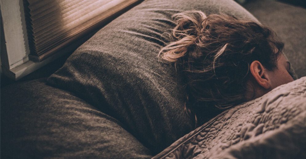 Woman sleeping on dark sheets, under a blanket.