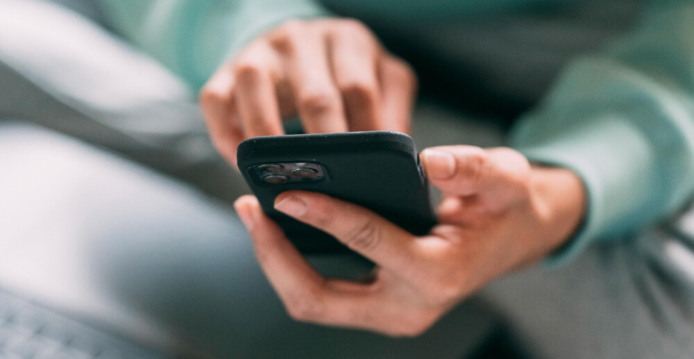 Closeup of hands holding and using a smartphone. The screen is out of view.