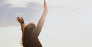 A woman with her hands flung into the air in celebration, silhouetted against the bright sky.