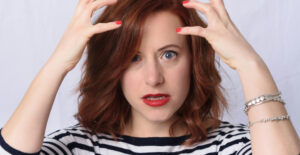 A woman with a distrurbed facial expression holds her hands near her head as though she wants to pull at her hair .