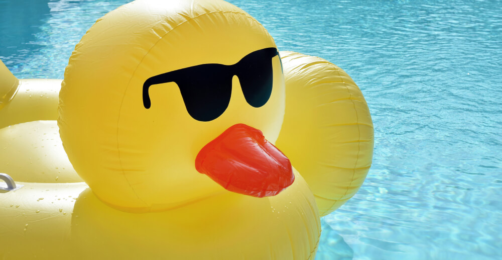 A large inflatable ppol floatie shaped like a rubber duck wearing sunglasses.