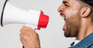 A man with brown skin and a short, dark beard yells into a magaphone