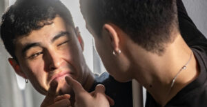 A young man is talking to himself in the mirror, pointing and making a fake-serious face.