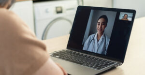 A woman using a laptop to have a video appointment with a female medical provider.