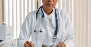 A female doctor at her desk. She wears a lab coat and stethoscope