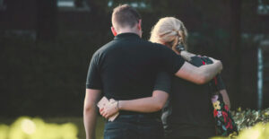 A man and woman with their arms around one another, viewed from behind