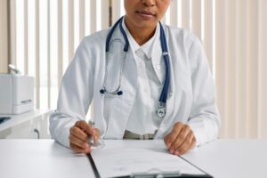 A female doctor at her desk. She wears a lab coat and stethoscope