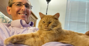 Tim with an orange cat lying contentedly on his stomach.