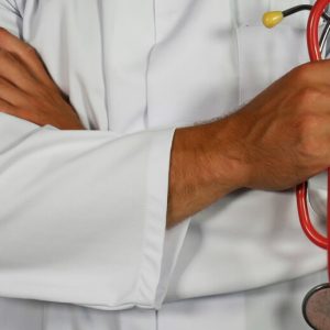 A male doctor in a white lab coat stands with his arms crossed, holding a stethoscope.