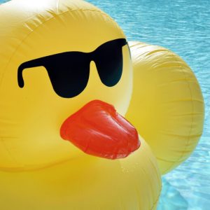 A large inflatable ppol floatie shaped like a rubber duck wearing sunglasses.