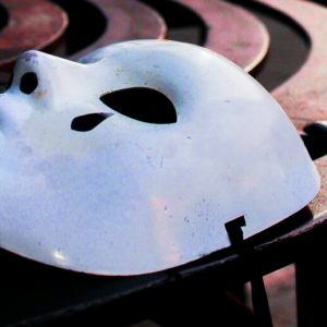 A white plastic tragedy mask discarded on a curved metal bench.