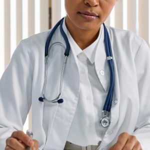 A female doctor at her desk. She wears a lab coat and stethoscope