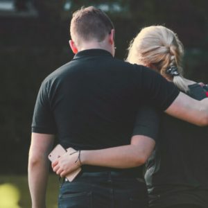 A man and woman with their arms around one another, viewed from behind