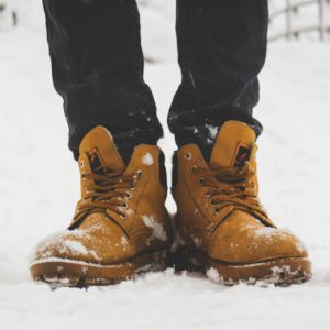 A person's feet in brown hiking boots, standing in the snow.