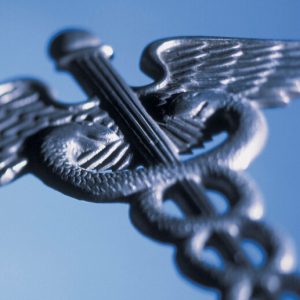 A silver-colored metal caduceus (the medical symbol that is two snakes wrapped around a winged staff) on a blue background.