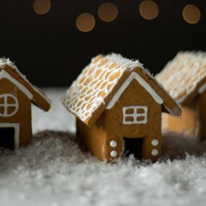 A row of small, simple gingerbread houses on a table strewn with fake snow.