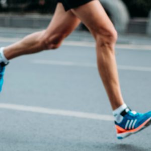 Legs of a person wearing shorts and sneakers running on a street. Recovery is a marathon
