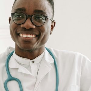 Young, Black, male doctor with a stethoscope around his neck smiles at someone off-camera