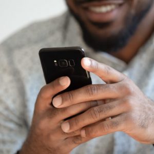 A Black man smiles as he uses a smartphone.