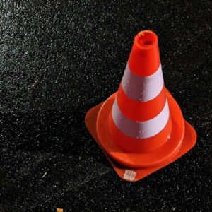 A bright orange safety cone sits on wet, shiny, black asphalt