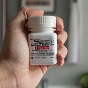 A hand holds a bottle of generic buprenorphine/naloxone medication