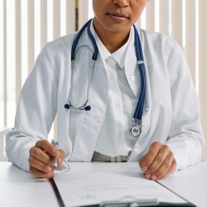 A female doctor at her desk. She wears a lab coat and stethoscope